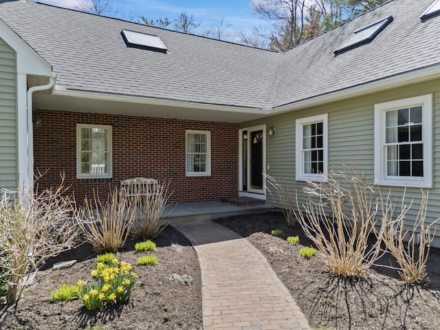 entrance to property featuring roof with shingles and brick siding