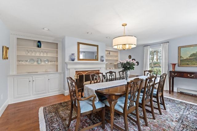 dining room featuring a baseboard radiator, wood finished floors, a brick fireplace, and built in features