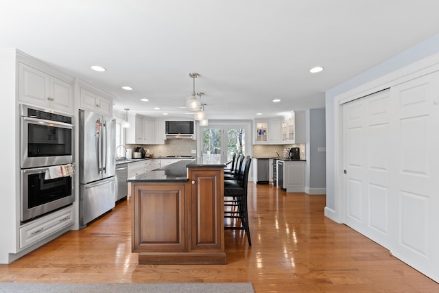 kitchen featuring stainless steel appliances, glass insert cabinets, a kitchen island, tasteful backsplash, and white cabinetry