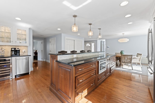 kitchen with brown cabinetry, wood-type flooring, appliances with stainless steel finishes, and beverage cooler