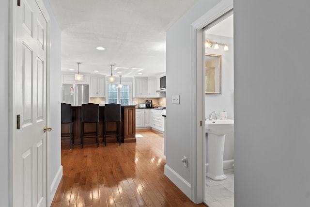 corridor featuring recessed lighting, light wood finished floors, baseboards, and a sink