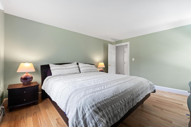 bedroom featuring a baseboard heating unit, baseboards, and wood finished floors