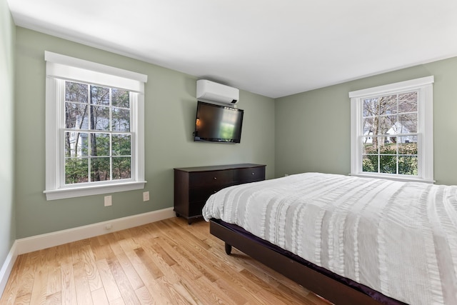 bedroom with multiple windows, light wood-style flooring, baseboards, and a wall mounted air conditioner