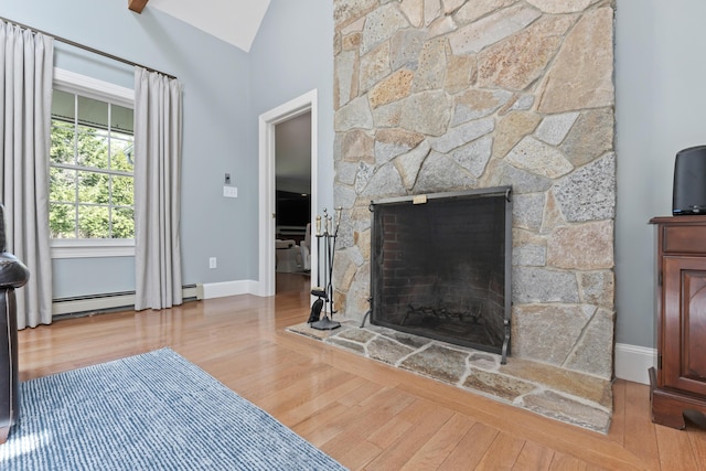 living room featuring baseboards, a stone fireplace, wood finished floors, and baseboard heating