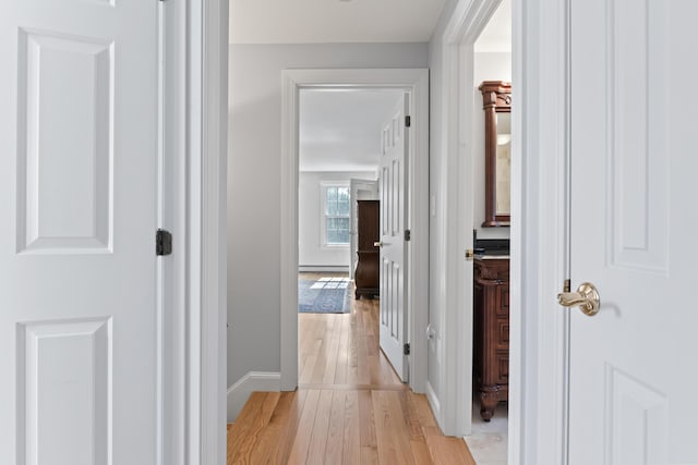 corridor with a baseboard radiator, baseboards, and light wood finished floors