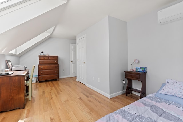 bedroom featuring a skylight, baseboards, a wall mounted AC, and light wood-type flooring