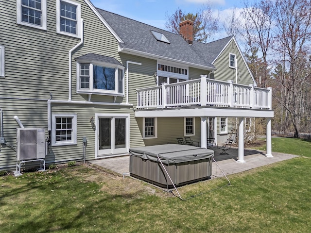rear view of house featuring a chimney, a patio, a lawn, roof with shingles, and a hot tub