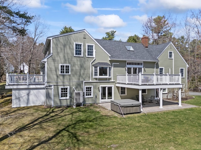back of house featuring a chimney, a yard, a wooden deck, a patio, and a hot tub