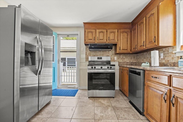 85 Tucker Ave, Portland, ME 04103 - kitchen with appliances with stainless steel finishes, under cabinet range hood, brown cabinets, decorative backsplash, and light tile patterned floors