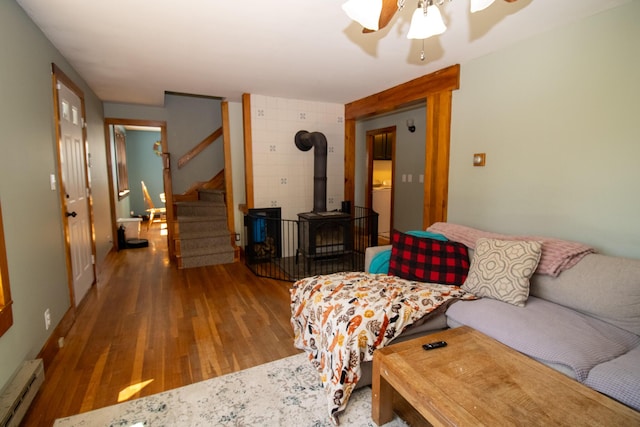 1114 Kennebec Rd, Hampden, ME 04444 - living area with stairway, wood finished floors, a wood stove, a ceiling fan, and a baseboard heating unit
