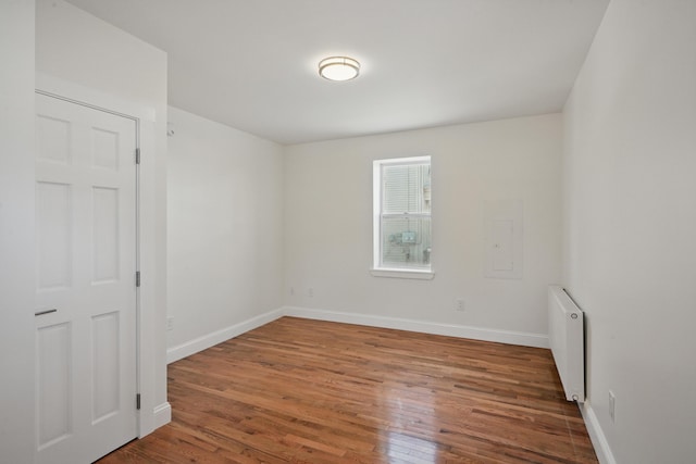 unfurnished room featuring radiator heating unit, wood finished floors, and baseboards
