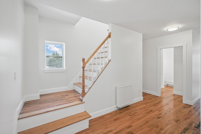 staircase with radiator heating unit, wood finished floors, and baseboards