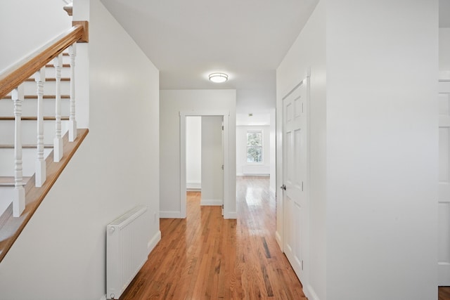 hall featuring radiator, light wood-style flooring, stairway, and baseboards