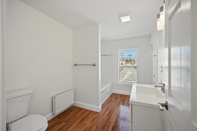 bathroom with radiator heating unit, wood-type flooring, toilet, baseboards, and vanity
