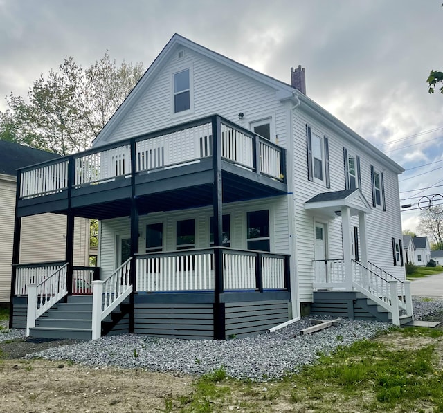 back of house with a balcony, covered porch, and a chimney