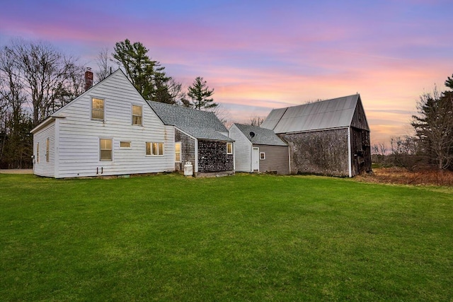 back of property with an outdoor structure, roof with shingles, a yard, and a chimney