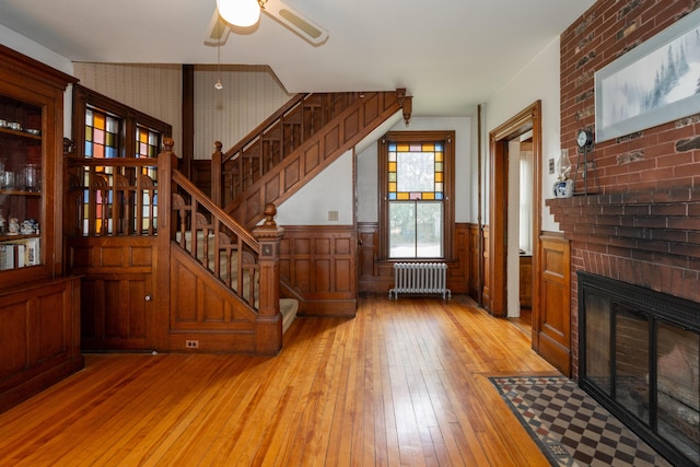 546 Main St, Westbrook, ME 04092 - unfurnished living room featuring radiator heating unit, light wood-style flooring, stairs, a ceiling fan, and wainscoting