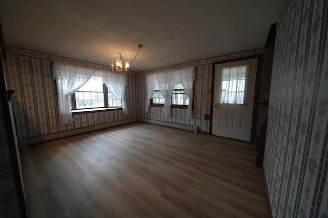 unfurnished dining area with wallpapered walls, wood finished floors, a chandelier, and plenty of natural light