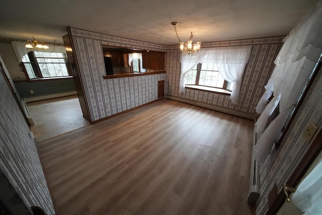 unfurnished dining area featuring wood finished floors, wallpapered walls, a baseboard heating unit, baseboards, and a notable chandelier