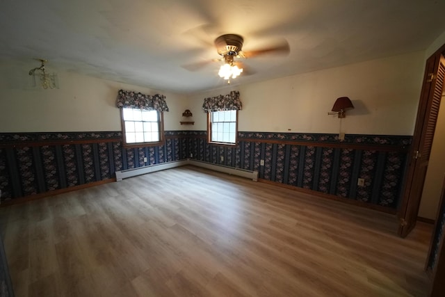 spare room featuring a wainscoted wall, wood finished floors, ceiling fan, and baseboard heating