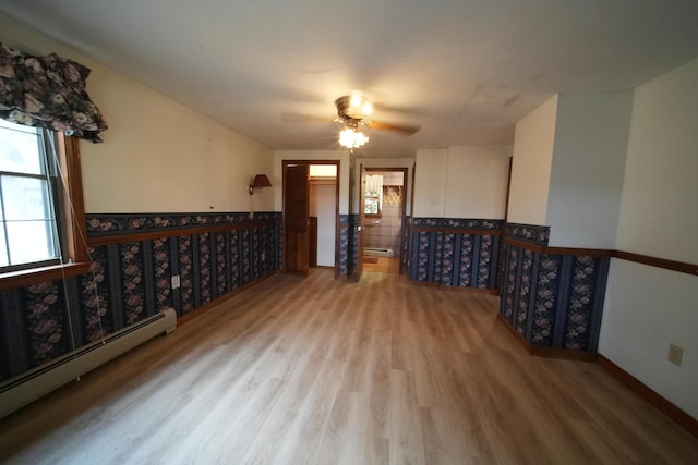empty room featuring baseboard heating, a baseboard radiator, wood finished floors, ceiling fan, and a wainscoted wall