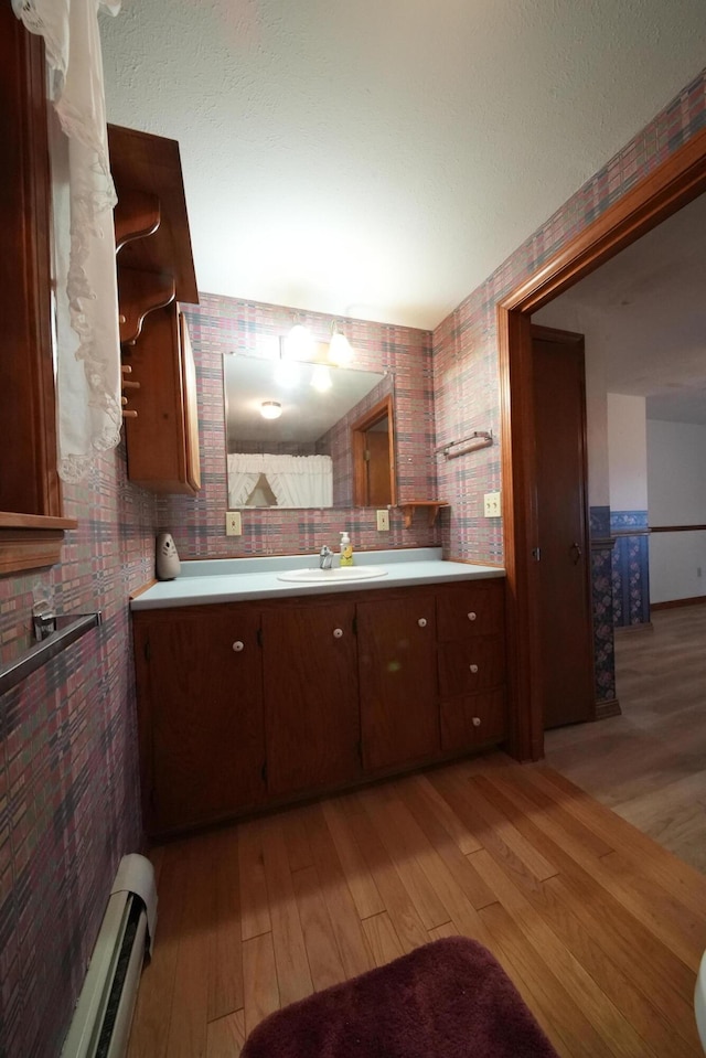 kitchen with a baseboard heating unit, light countertops, light wood-type flooring, and a sink