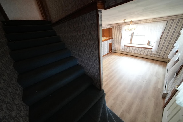 stairs featuring a chandelier, wallpapered walls, wood finished floors, and baseboard heating