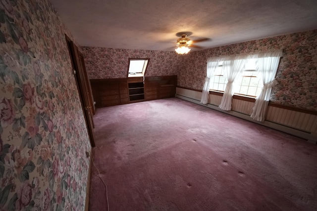 additional living space featuring wallpapered walls, a wealth of natural light, baseboard heating, and wainscoting