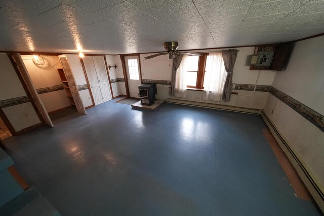 below grade area featuring baseboard heating, a ceiling fan, a wood stove, and a wall mounted AC