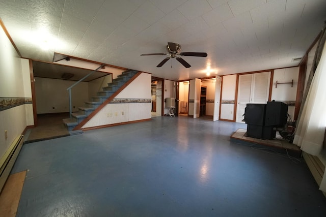 unfurnished living room with stairway, concrete floors, a ceiling fan, a baseboard heating unit, and a wood stove