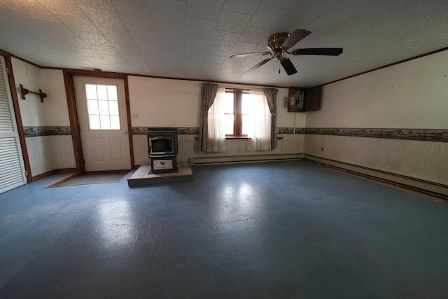 unfurnished living room featuring a wood stove, a healthy amount of sunlight, ceiling fan, and wainscoting
