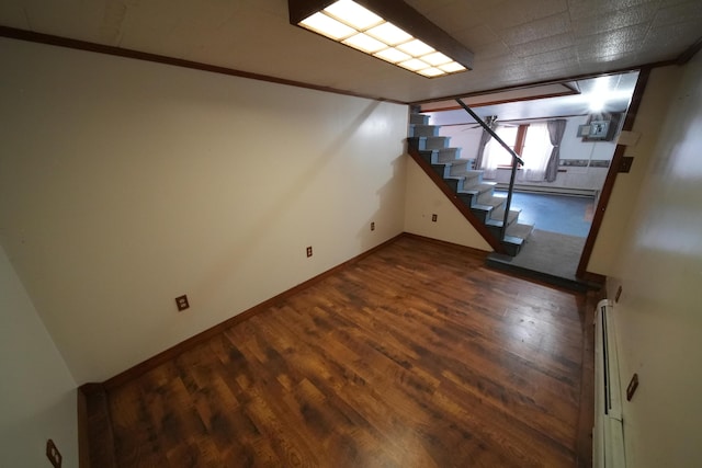 basement featuring a baseboard heating unit, dark wood finished floors, stairway, and baseboards