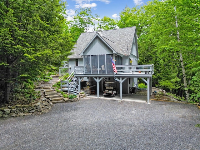 view of front of home with a carport, stairs, aphalt driveway, a shingled roof, and a sunroom
