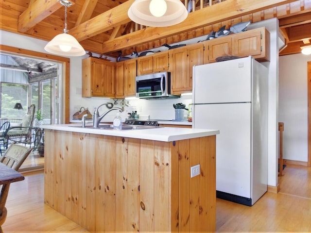 kitchen with light wood-style flooring, stainless steel microwave, freestanding refrigerator, decorative light fixtures, and light countertops