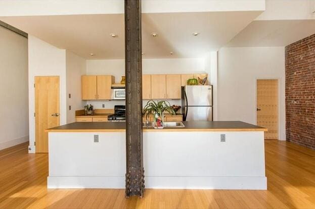 15 Brown St Unit 205, Portland, ME 04101 - kitchen with stainless steel appliances, light wood-style floors, dark countertops, light brown cabinets, and brick wall