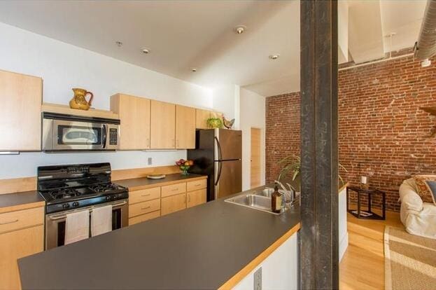 15 Brown St Unit 205, Portland, ME 04101 - kitchen featuring appliances with stainless steel finishes, light brown cabinetry, a sink, dark countertops, and brick wall