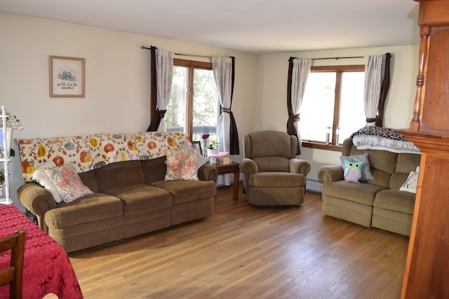 living area with a healthy amount of sunlight, baseboard heating, and light wood finished floors