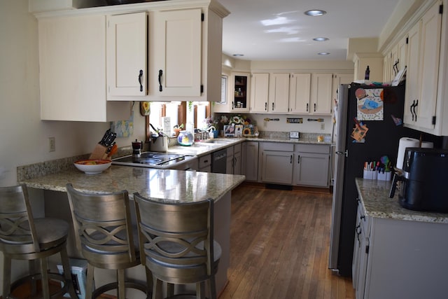 kitchen with a peninsula, light stone counters, a sink, dark wood finished floors, and dishwasher