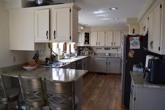 kitchen with a peninsula, black dishwasher, dark wood-type flooring, light stone counters, and a sink