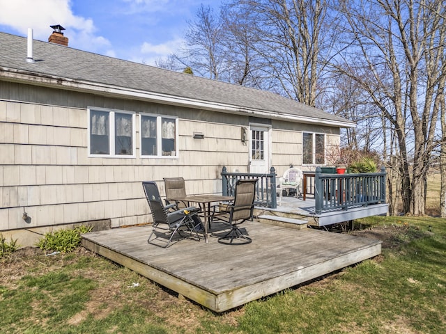 rear view of property featuring a shingled roof, a wooden deck, outdoor dining area, a chimney, and a yard
