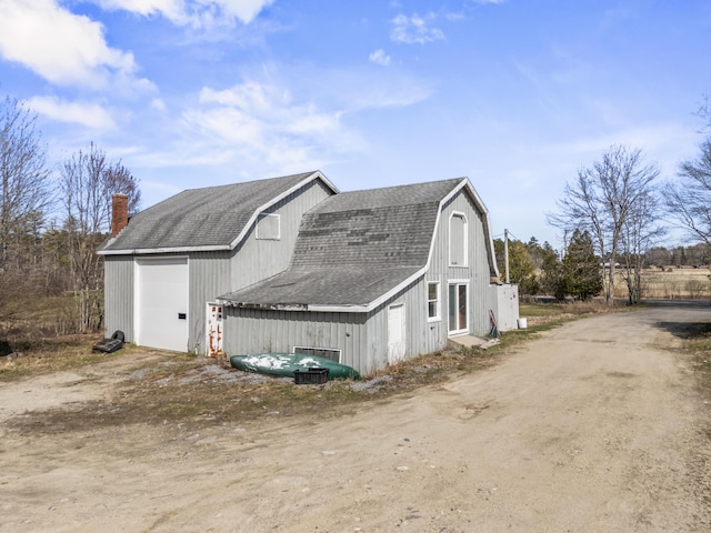 view of side of home featuring a garage, a gambrel roof, roof with shingles, and a chimney