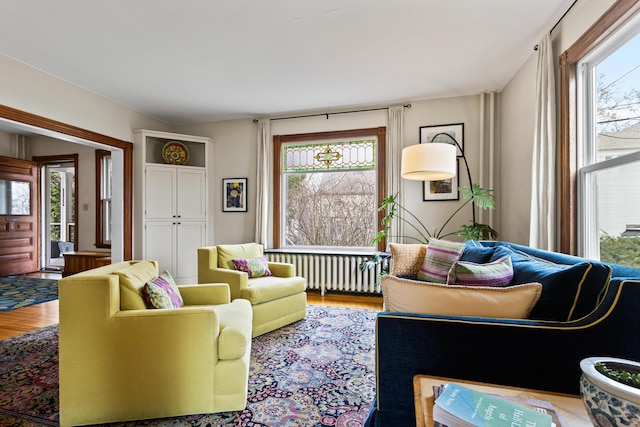 living room with radiator heating unit, wood finished floors, and a healthy amount of sunlight
