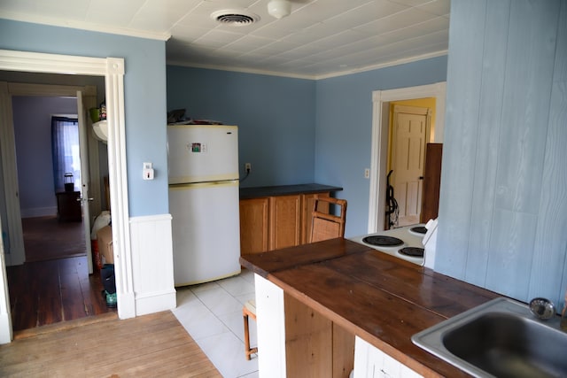 kitchen featuring visible vents, a sink, freestanding refrigerator, crown molding, and light wood-style flooring