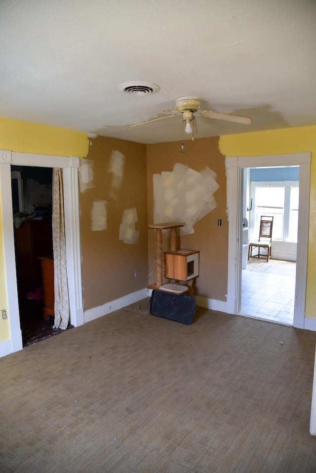 unfurnished living room with carpet floors, visible vents, a ceiling fan, and baseboards