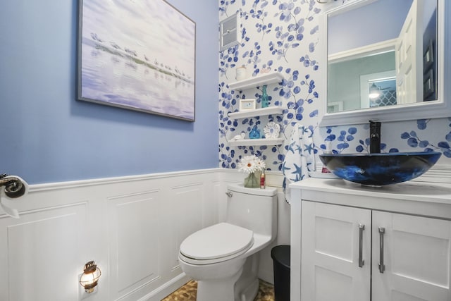 bathroom featuring wainscoting, toilet, vanity, and a decorative wall