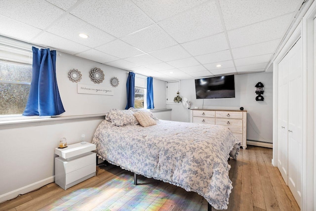 bedroom featuring baseboards, wood finished floors, a drop ceiling, and baseboard heating