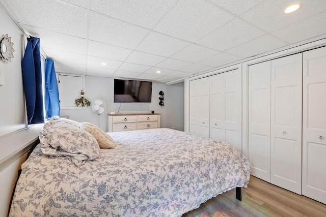 bedroom featuring recessed lighting, wood finished floors, two closets, and a paneled ceiling