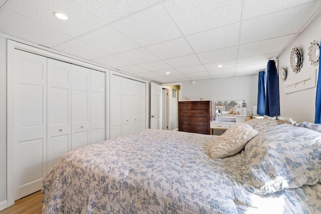 bedroom featuring recessed lighting, multiple closets, a paneled ceiling, and light wood-style flooring