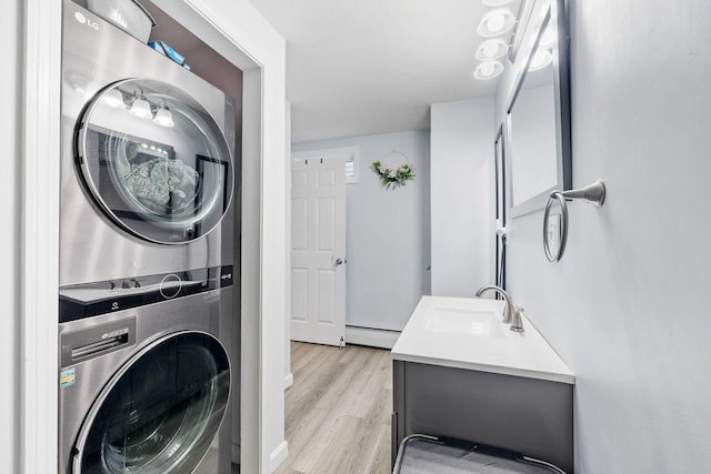 laundry area featuring a baseboard heating unit, a sink, light wood-type flooring, stacked washing maching and dryer, and laundry area
