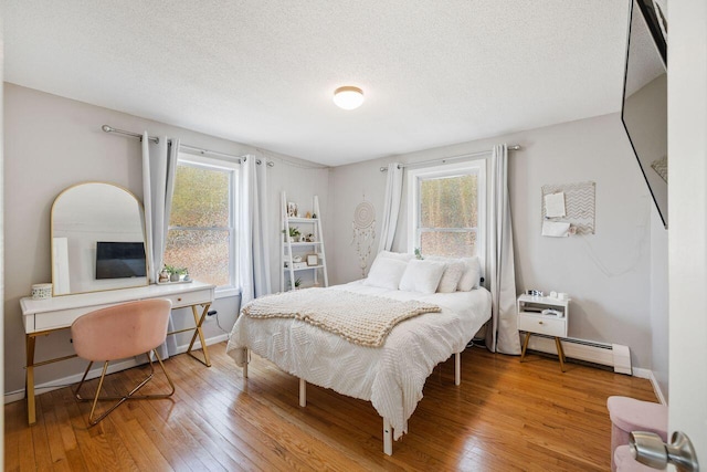 bedroom with a baseboard heating unit, hardwood / wood-style floors, a textured ceiling, and multiple windows